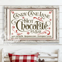 Candy cane lane hot chocolate bar sign in a christmas scene with a bench and a christmas tree