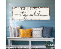 a bench with pillows and a sign that says get cozy stay awhile