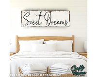 a bed with white linens and a wooden sign that says sweet dreams