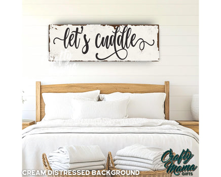 a bed with white linens and a wooden sign that says let&#39;s cu