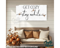 a picture of a couch with pillows and a sign that says get cozy stay awhile