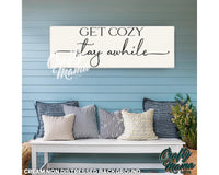 a bench with pillows and a sign that says get cozy stay awhile