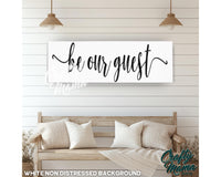 a sign that says be our guest hanging on a wall